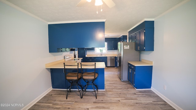 kitchen featuring blue cabinets, appliances with stainless steel finishes, hardwood / wood-style floors, and a breakfast bar area