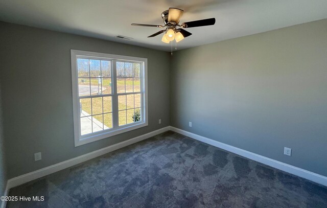 spare room with ceiling fan, dark colored carpet, visible vents, and baseboards