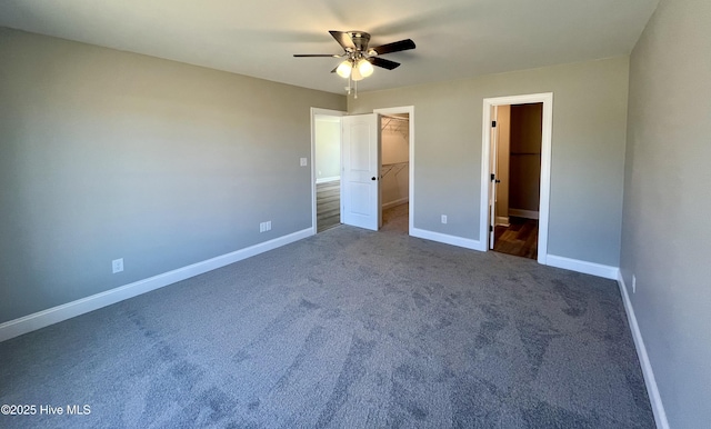 unfurnished bedroom featuring baseboards, a ceiling fan, a walk in closet, dark carpet, and a closet