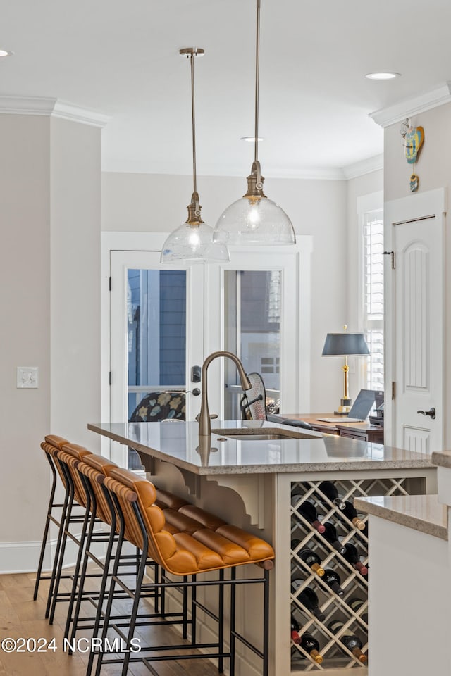 kitchen with light stone counters, sink, crown molding, decorative light fixtures, and a kitchen breakfast bar