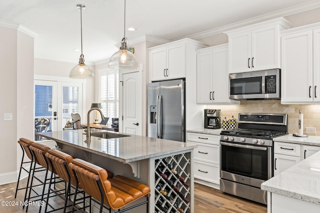 kitchen with light hardwood / wood-style floors, pendant lighting, a center island with sink, white cabinets, and appliances with stainless steel finishes