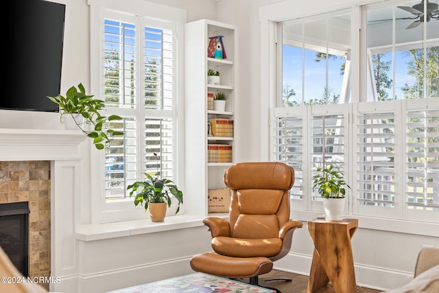 living area with a tiled fireplace, wood-type flooring, a wealth of natural light, and ceiling fan