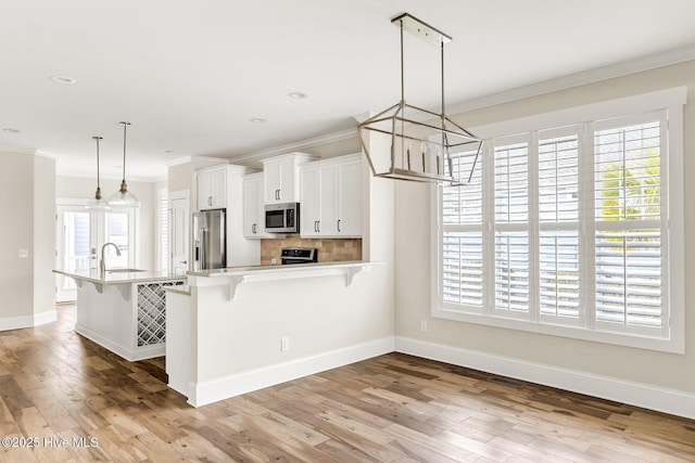 kitchen with a kitchen bar, crown molding, hanging light fixtures, stainless steel appliances, and white cabinets