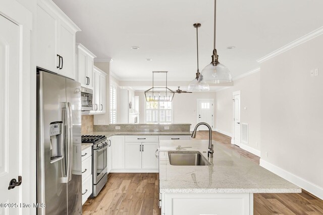 kitchen featuring appliances with stainless steel finishes, sink, white cabinets, hanging light fixtures, and light stone countertops