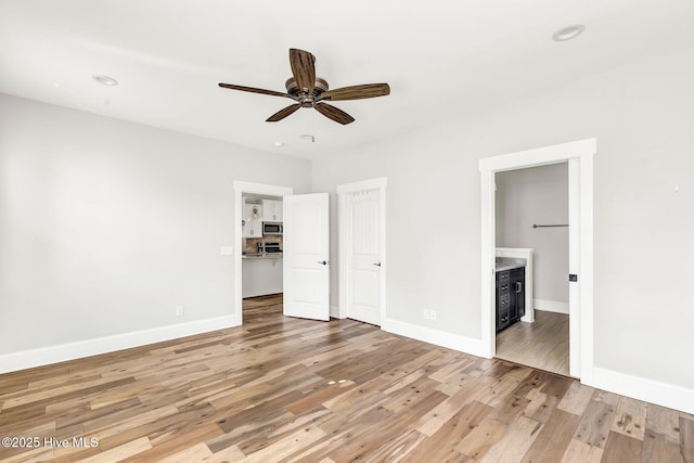 unfurnished bedroom featuring ensuite bathroom, a spacious closet, light hardwood / wood-style flooring, a closet, and ceiling fan