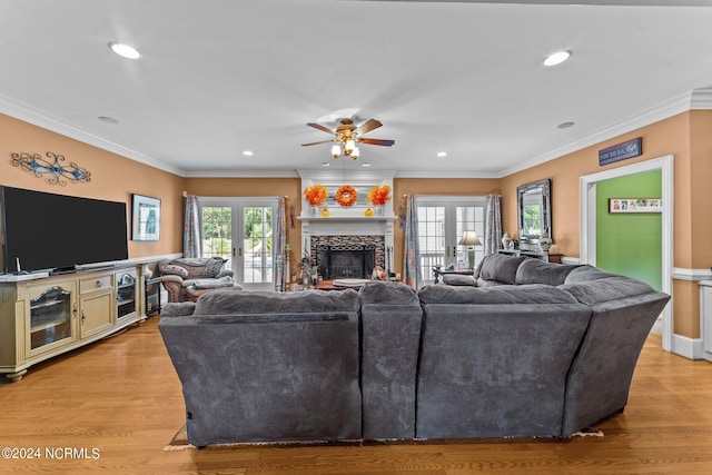 living area featuring light wood-style floors, ornamental molding, a stone fireplace, and french doors