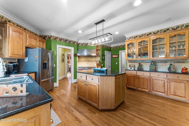 kitchen featuring wood finished floors, a sink, wall chimney exhaust hood, glass insert cabinets, and crown molding