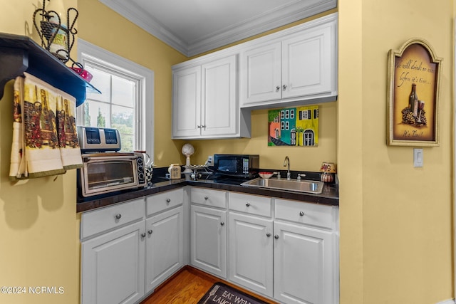 kitchen featuring black microwave, a toaster, dark countertops, white cabinetry, and a sink