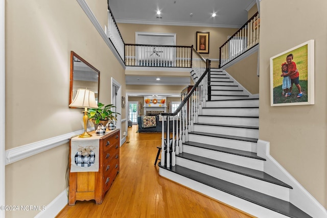 entryway featuring a high ceiling, a fireplace, wood finished floors, stairway, and crown molding