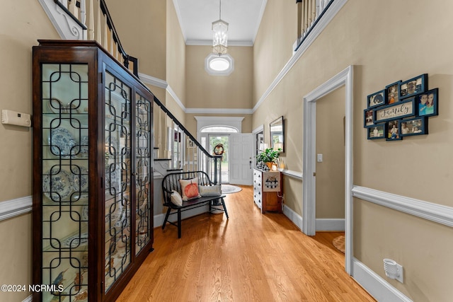 foyer featuring baseboards, a towering ceiling, stairway, wood finished floors, and crown molding