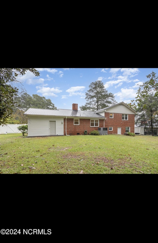back of property with a lawn, a chimney, fence, and metal roof
