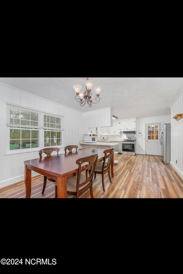 dining space featuring light wood-type flooring, a textured ceiling, and an inviting chandelier