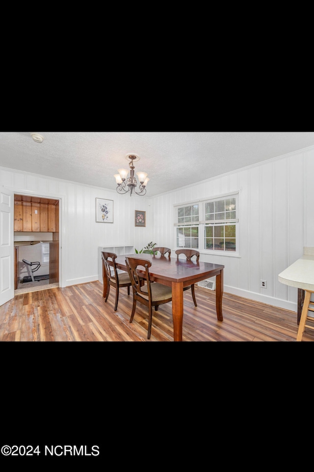 dining space with an inviting chandelier, light wood-type flooring, and a textured ceiling