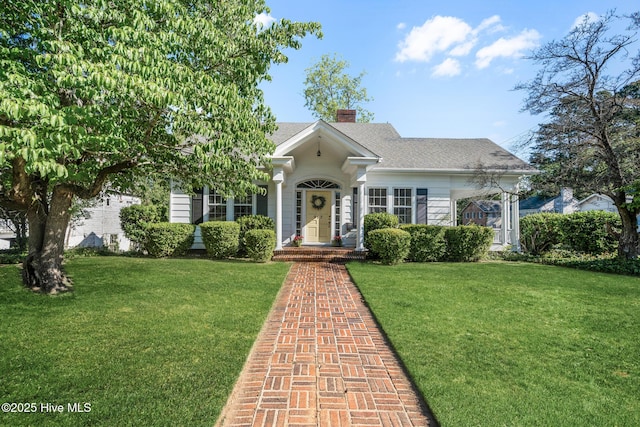 view of front of home with roof with shingles, a chimney, and a front yard