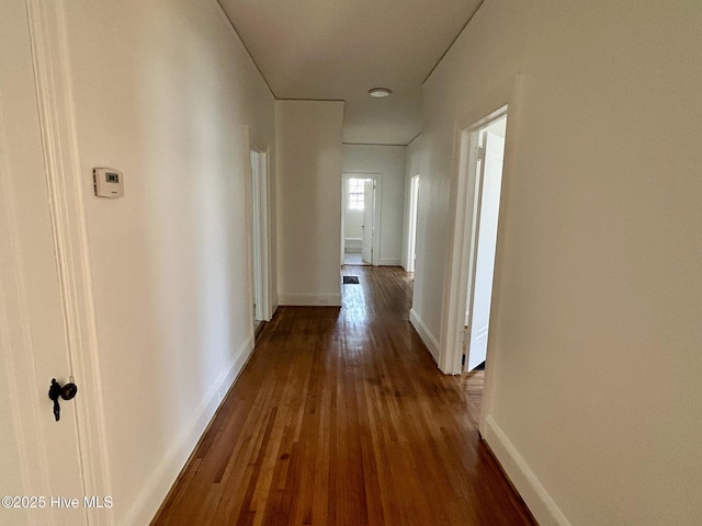 corridor featuring baseboards and dark wood-style floors