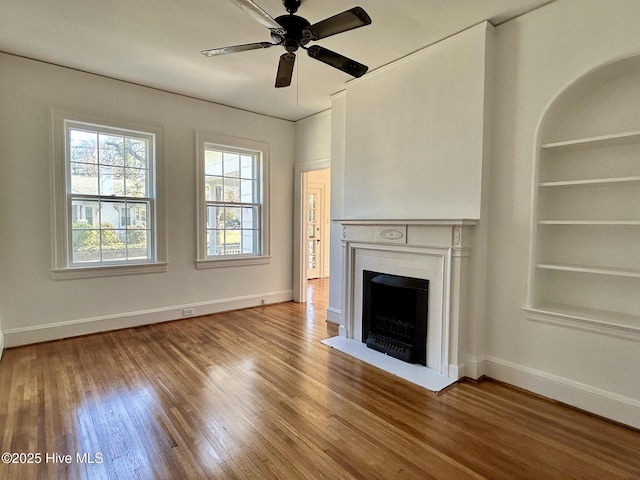 unfurnished living room featuring a brick fireplace, built in shelves, ceiling fan, and hardwood / wood-style flooring