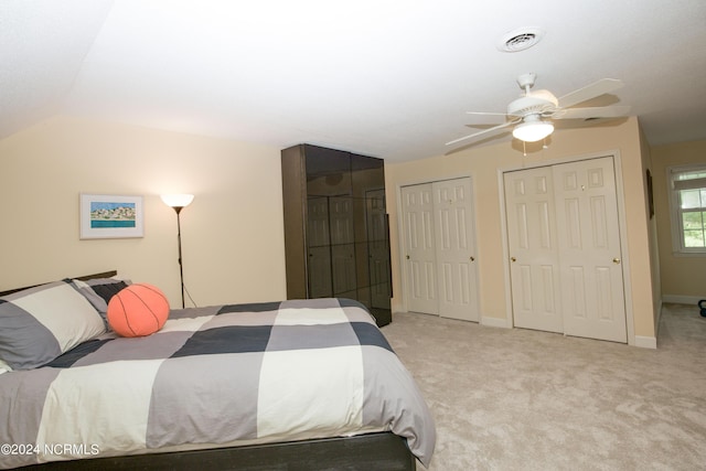 bedroom featuring light colored carpet, a ceiling fan, lofted ceiling, and two closets