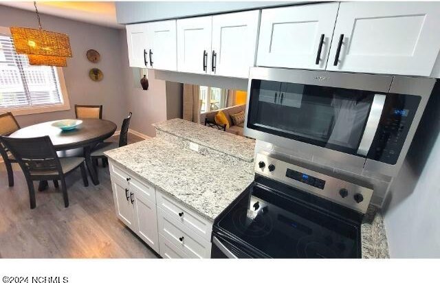10166 Beach Dr SW Unit 5306, Calabash, NC 28467 - kitchen with appliances with stainless steel finishes, white cabinetry, light wood-style floors, hanging light fixtures, and light stone counters