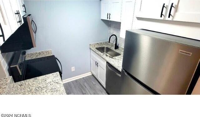 10166 Beach Dr SW Unit 5306, Calabash, NC 28467 - kitchen with dishwashing machine, stainless steel fridge, white cabinetry, light stone countertops, and wood finished floors