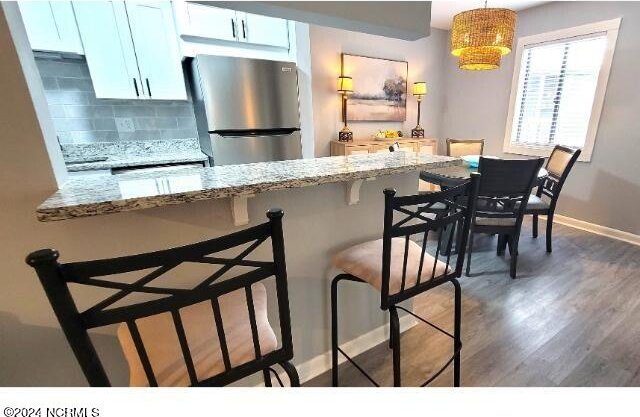 10166 Beach Dr SW Unit 5306, Calabash, NC 28467 - kitchen featuring freestanding refrigerator, wood finished floors, backsplash, a breakfast bar area, and light stone counters