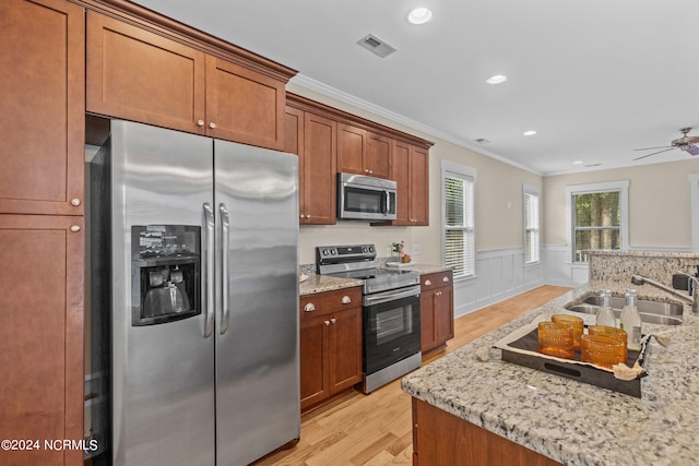 kitchen with ornamental molding, appliances with stainless steel finishes, light stone countertops, sink, and light hardwood / wood-style floors