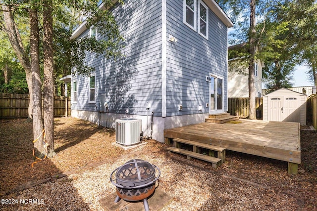 view of side of property with central AC unit, an outdoor fire pit, a storage unit, and a deck