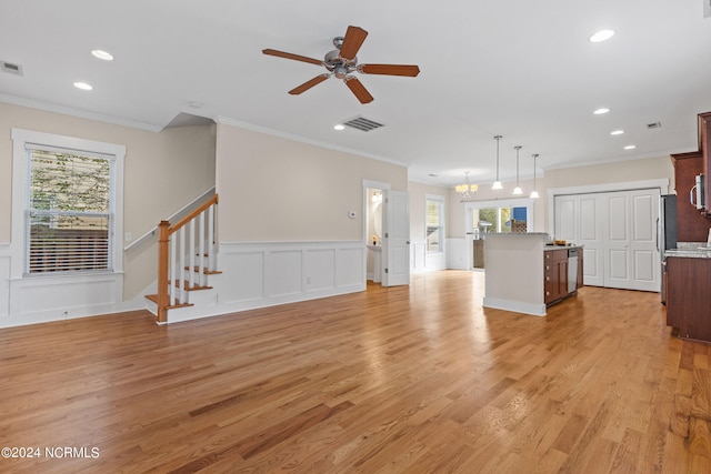 unfurnished living room with light hardwood / wood-style floors, ceiling fan with notable chandelier, a healthy amount of sunlight, and ornamental molding