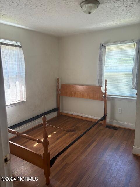 unfurnished bedroom with a textured ceiling and dark hardwood / wood-style flooring