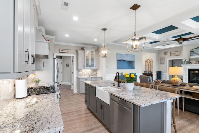 kitchen with hanging light fixtures, an island with sink, ceiling fan with notable chandelier, stainless steel appliances, and sink