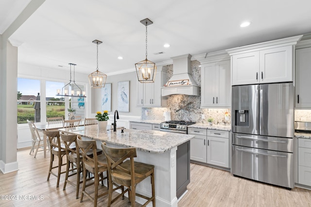 kitchen with a kitchen island with sink, a breakfast bar area, custom exhaust hood, appliances with stainless steel finishes, and light stone countertops