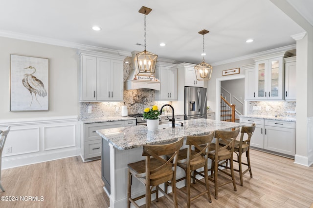 kitchen featuring pendant lighting, stainless steel fridge with ice dispenser, an island with sink, light hardwood / wood-style flooring, and light stone countertops