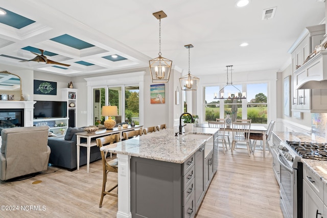 kitchen with ceiling fan with notable chandelier, high end stainless steel range oven, pendant lighting, and an island with sink