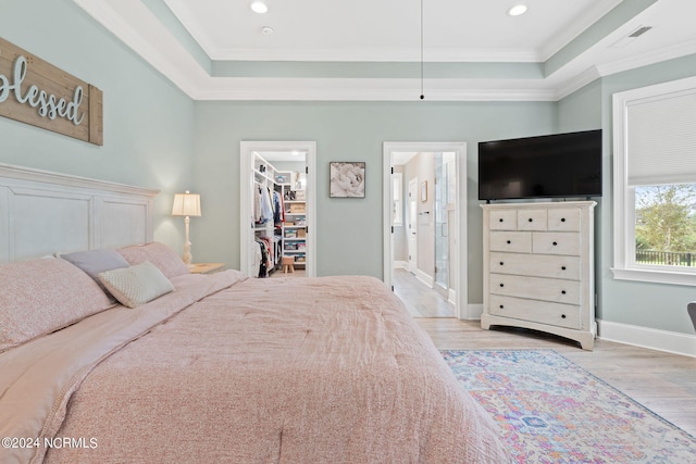 bedroom with a closet, light hardwood / wood-style flooring, ornamental molding, and a walk in closet