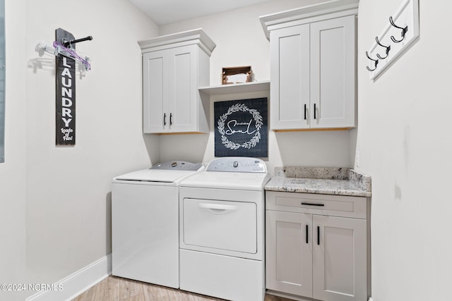 clothes washing area with cabinets, light hardwood / wood-style flooring, and washing machine and clothes dryer