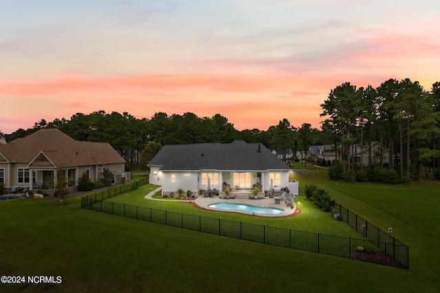 back house at dusk featuring a patio, a fenced in pool, and a yard