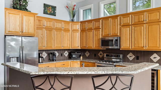 kitchen featuring kitchen peninsula, appliances with stainless steel finishes, light stone countertops, and a kitchen breakfast bar