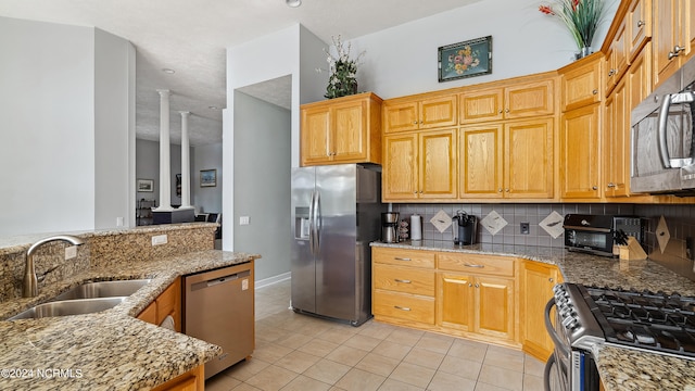 kitchen featuring stainless steel appliances, light tile patterned floors, stone counters, decorative backsplash, and sink