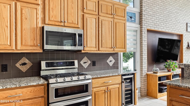 kitchen featuring stainless steel appliances, light tile patterned flooring, light stone counters, backsplash, and beverage cooler