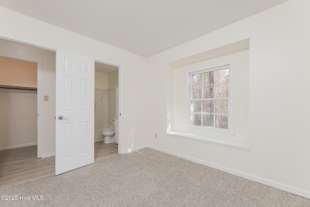 unfurnished bedroom featuring a walk in closet, connected bathroom, carpet flooring, and a closet