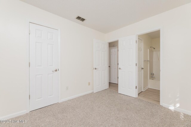 unfurnished bedroom with ensuite bath, a walk in closet, a closet, and wood-type flooring