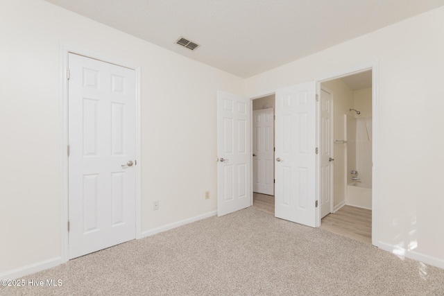 unfurnished bedroom with ensuite bathroom and light colored carpet