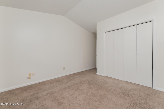 unfurnished bedroom featuring vaulted ceiling, light colored carpet, and a closet