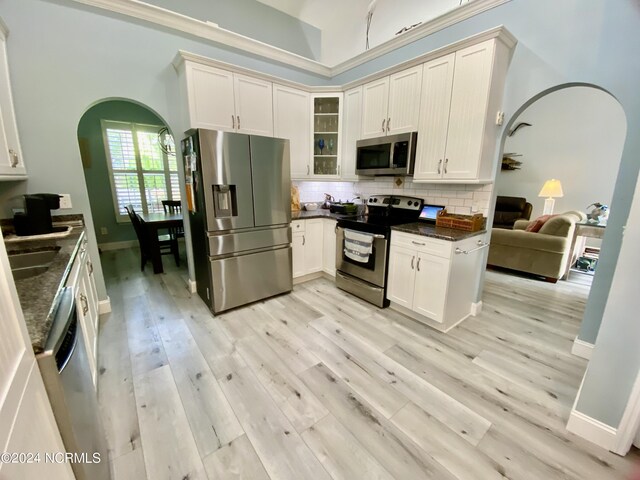 kitchen featuring light hardwood / wood-style flooring, a high ceiling, decorative backsplash, and appliances with stainless steel finishes