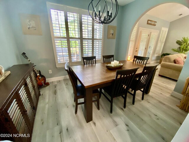 dining space featuring light wood-type flooring, a healthy amount of sunlight, and an inviting chandelier