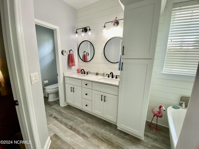 bathroom with vanity, a tub, wooden walls, hardwood / wood-style flooring, and toilet