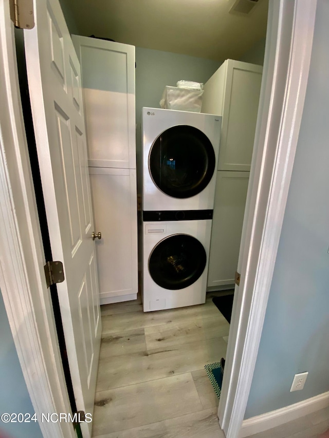 laundry area featuring stacked washer and dryer, light hardwood / wood-style flooring, and cabinets