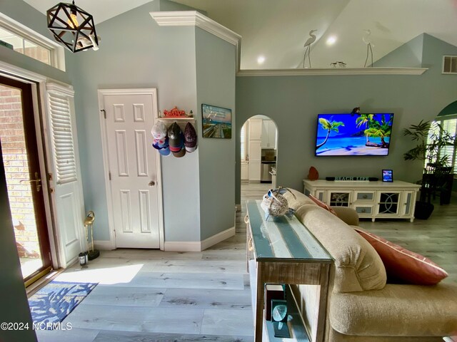 interior space with light wood-type flooring, crown molding, a chandelier, and high vaulted ceiling