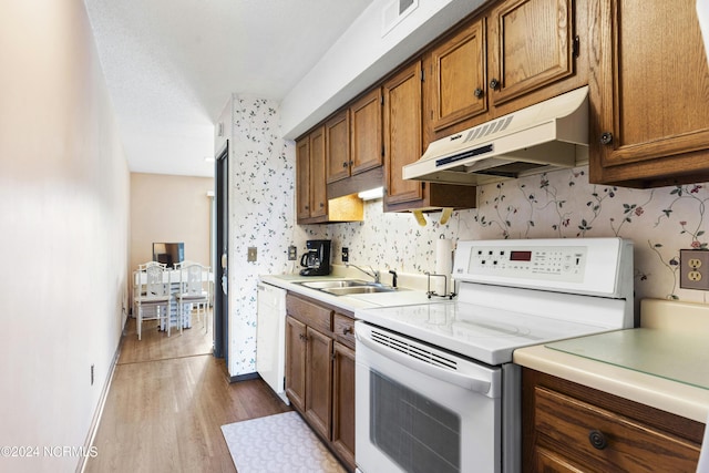 kitchen with sink, a textured ceiling, white appliances, and light hardwood / wood-style flooring