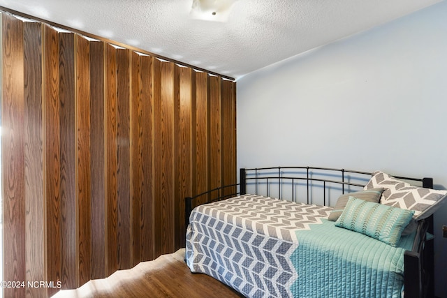 bedroom with wooden walls, hardwood / wood-style floors, and a textured ceiling