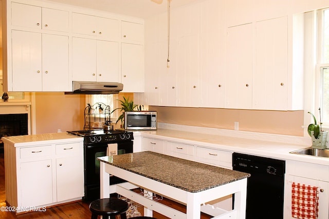 kitchen with a brick fireplace, white cabinets, dark wood-type flooring, and black appliances